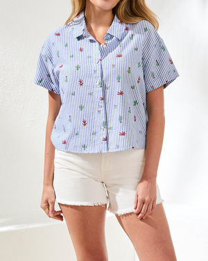 Woman wearing a blue and white striped shirt with floral patterns and white shorts on a white background