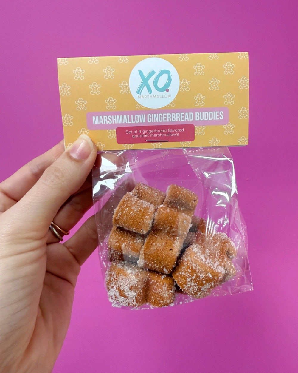 Hand holding a package of marshmallow gingerbread buddies against a pink background