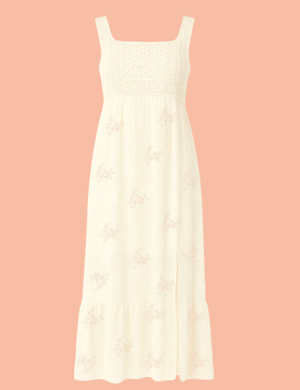 A sleeveless cream lace dress with a textured embroidered bodice and ruffled hem, hanging on a black hanger against a white wall next to a dark green velvet chair.