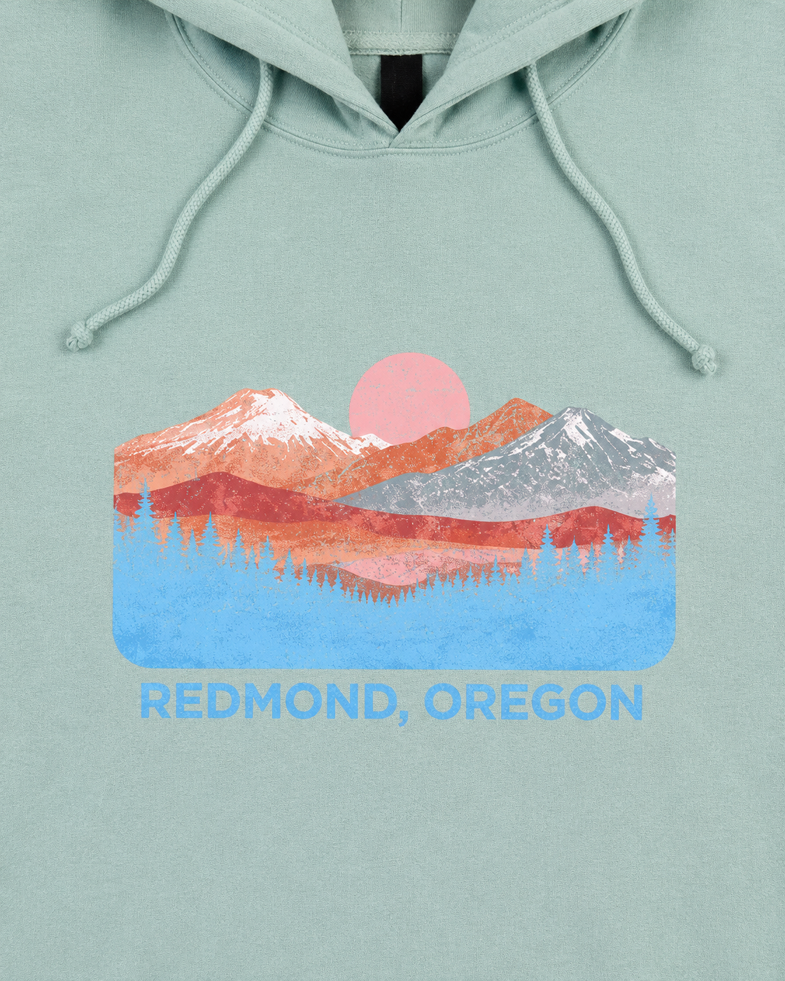 A mint green pullover hoodie with a colorful graphic of a mountain sunset and the text 'REDMOND, OREGON' printed on the chest, displayed on a clean white background.