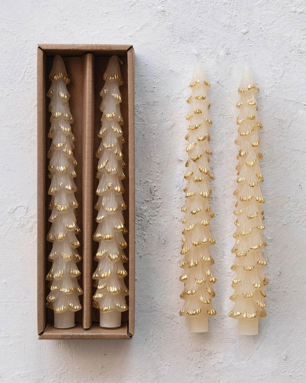 Two decorative candles with gold accents on a textured white surface, one in a box.