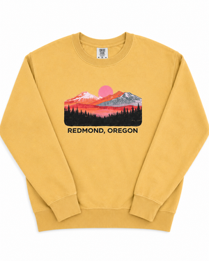 A mustard yellow crewneck sweatshirt featuring a colorful mountain sunset graphic with the text 'REDMOND, OREGON' printed below it, displayed on a clean white background.