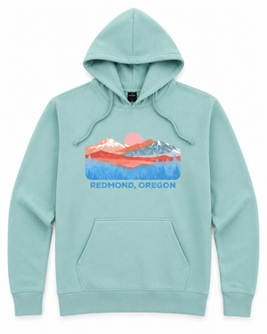 A mint green pullover hoodie with a colorful graphic of a mountain sunset and the text 'REDMOND, OREGON' printed on the chest, displayed on a clean white background.