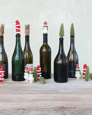Decorative wine bottles with Christmas-themed bottle stoppers on a wooden surface.