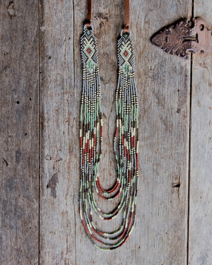 A long beaded necklace with multiple strands hanging from a brown leather strap, displayed against a rustic weathered wood background.