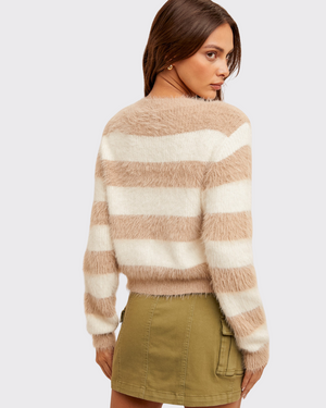 Woman wearing a beige and white striped sweater with a plain background