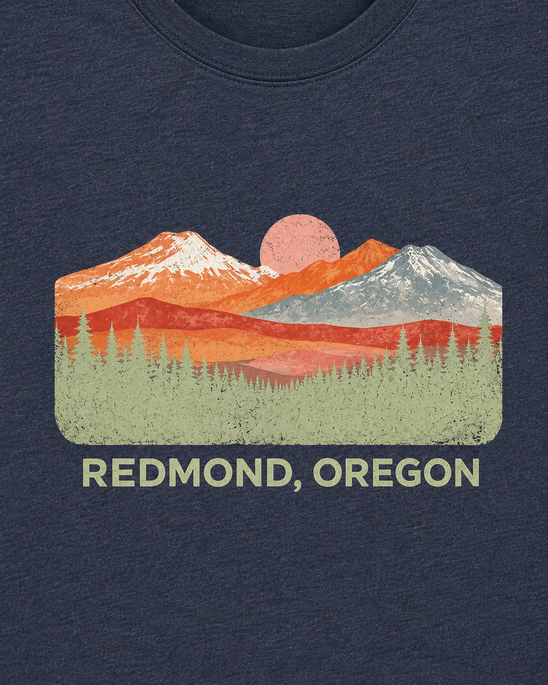 A heather navy blue short-sleeve t-shirt with a colorful graphic of mountains, a pink sun, and the text 'REDMOND, OREGON' printed on the chest.