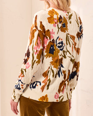 Woman wearing a floral blouse and brown pants with a blurred background
