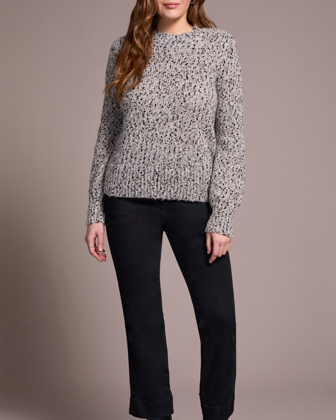Woman wearing a patterned sweater and black pants against a neutral background