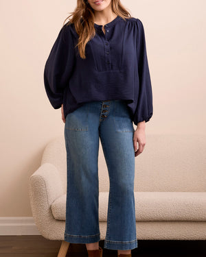 Person wearing a navy blouse, blue jeans, and brown boots standing in a room with a beige sofa.